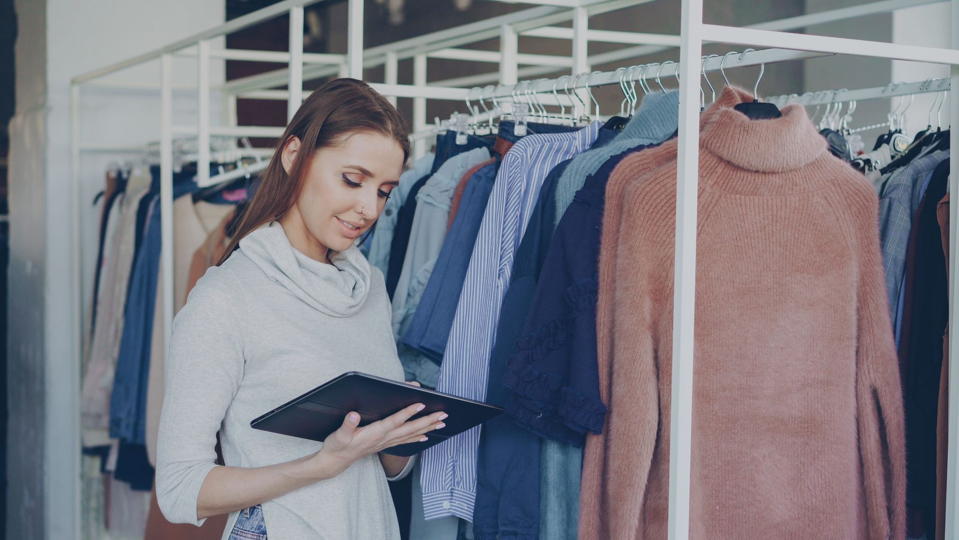 衣料を並べた店内で、タブレットを手に在庫と発注の内容を確認している店舗スタッフ